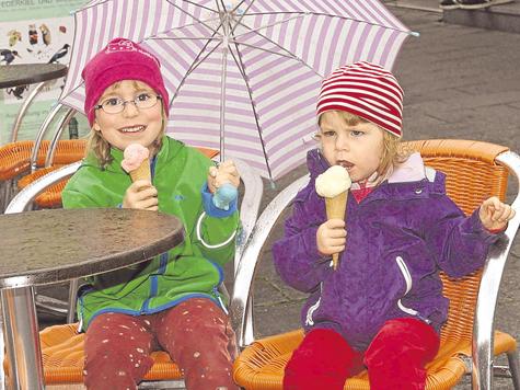 Eis unterm Schirm und mit M&uuml;tze: Franziska (l.), f&uuml;nfeinhalb Jahre alt, l&auml;sst sich die Laune vom Wetter nicht vermiesen. Ihre kleine Schwester Johanna, zweieinhalb, isst das Eis offenbar eher widerwillig &ndash; und macht ein Gesicht wie drei Tage Regenwetter. Foto: be